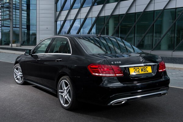 Mercedes-Benzes e 350 negro aparcado en la carretera junto al edificio de oficinas