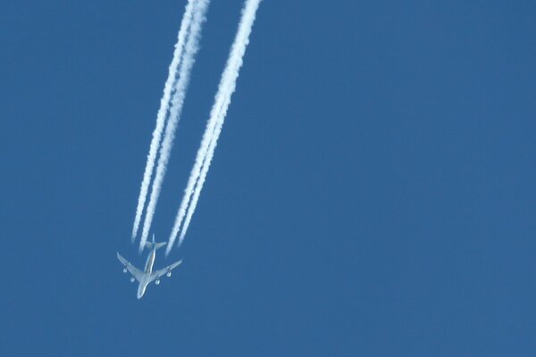 El avión vuela en el cielo azul dejando un rastro blanco