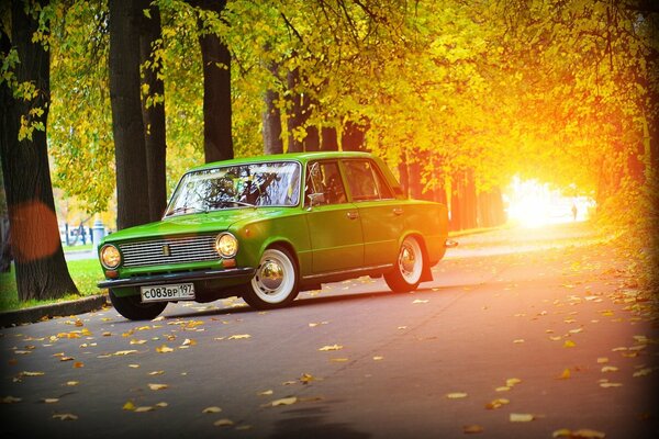 Coche verde Lada en el fondo de la carretera de otoño