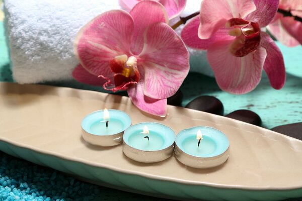 Tres velas encendidas. En el fondo una toalla blanca y orquídeas