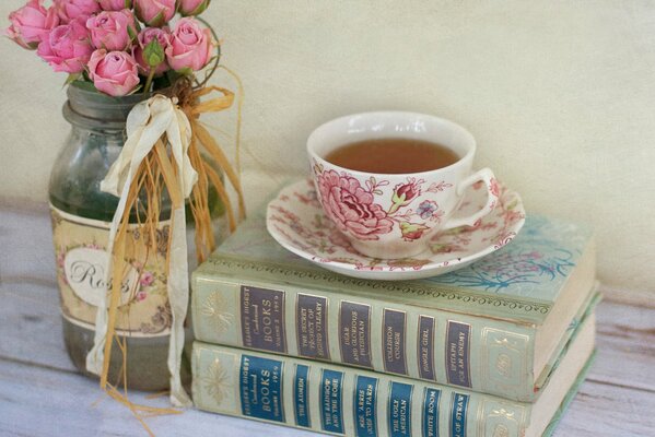 Un ramo de rosas Rosadas en un frasco y libros junto a una taza de té