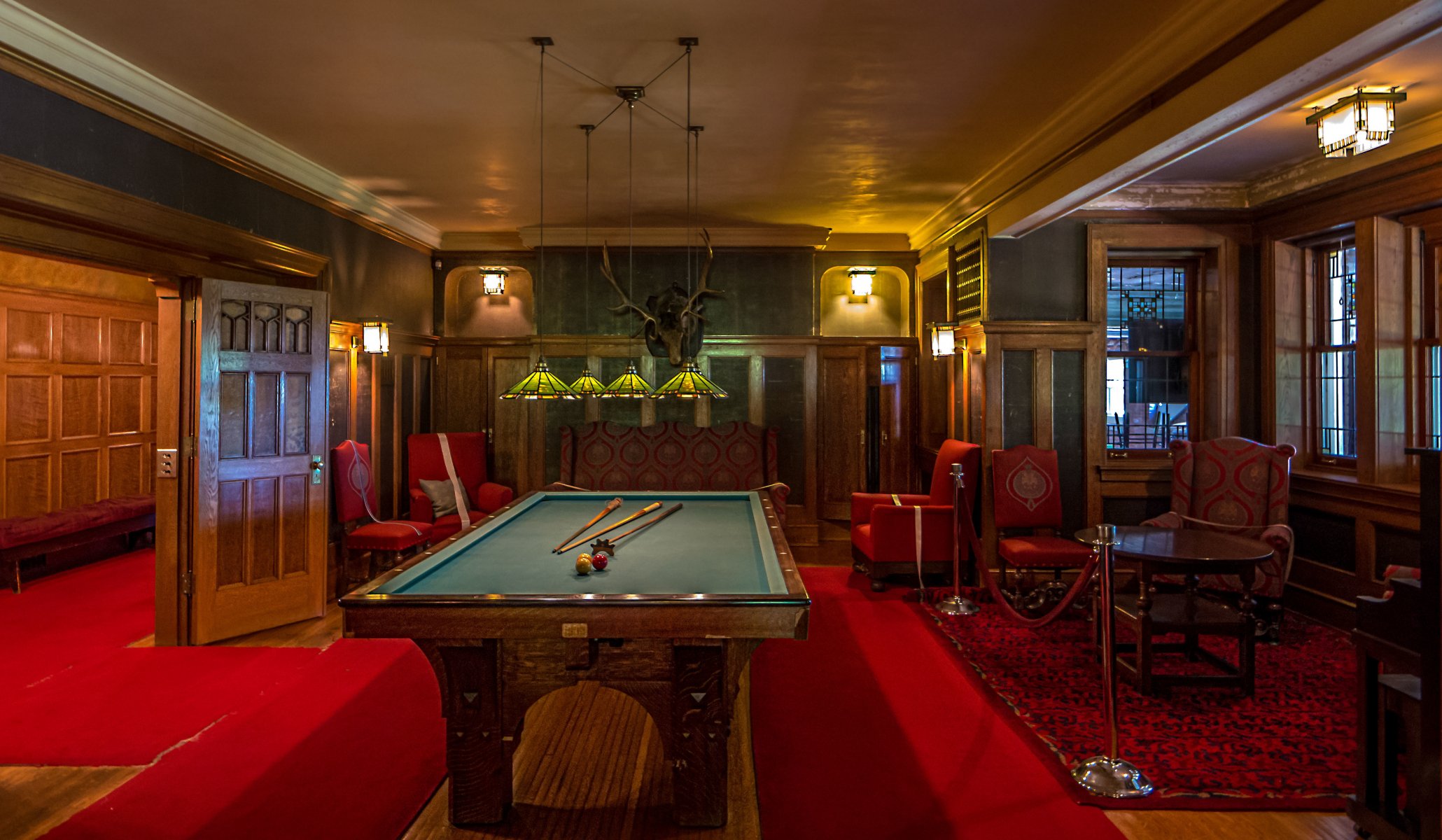 billar araña alfombra roja cabeza de alce sillón mesa ventanas luz